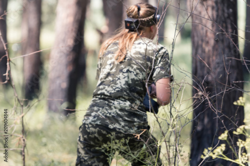 Girl in camouflage with a gun, plays laser tag in the forest. the player is aiming. Lasertag shooting game in open air. Military sport. Simulation of military operations. blur
