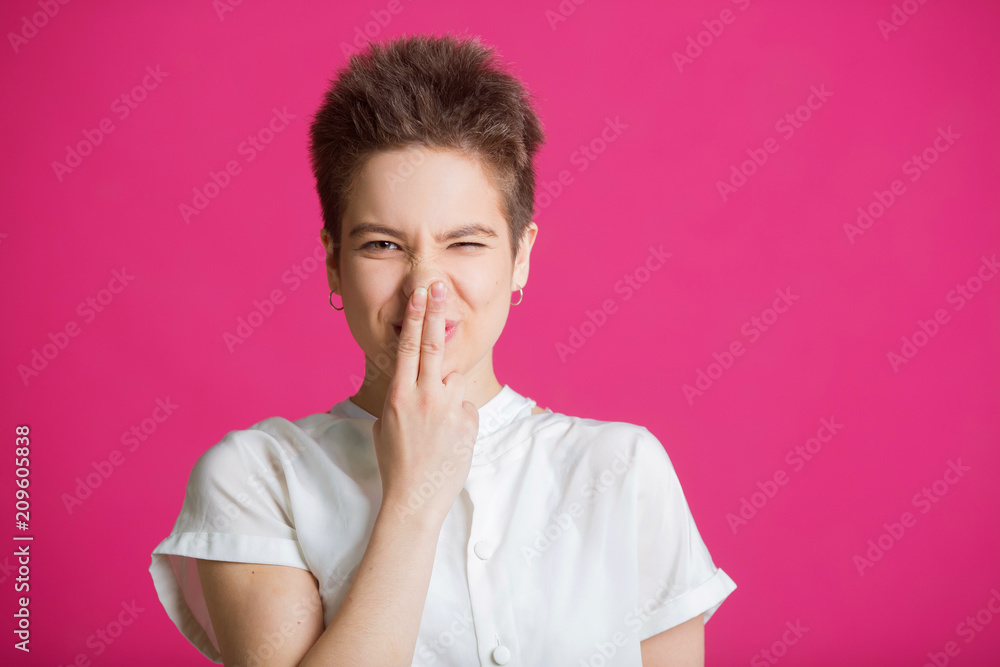 beautiful young girl with short hairdo in a white t-shirt on a pink background with facial expressions on her face beautiful young girl with short hairdo in a white t-shirt on a pink background with facial expressions on her face