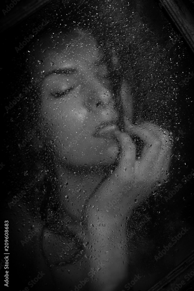 Portrait of a passionate, wet, sexy girl behind a glass with drops of water
