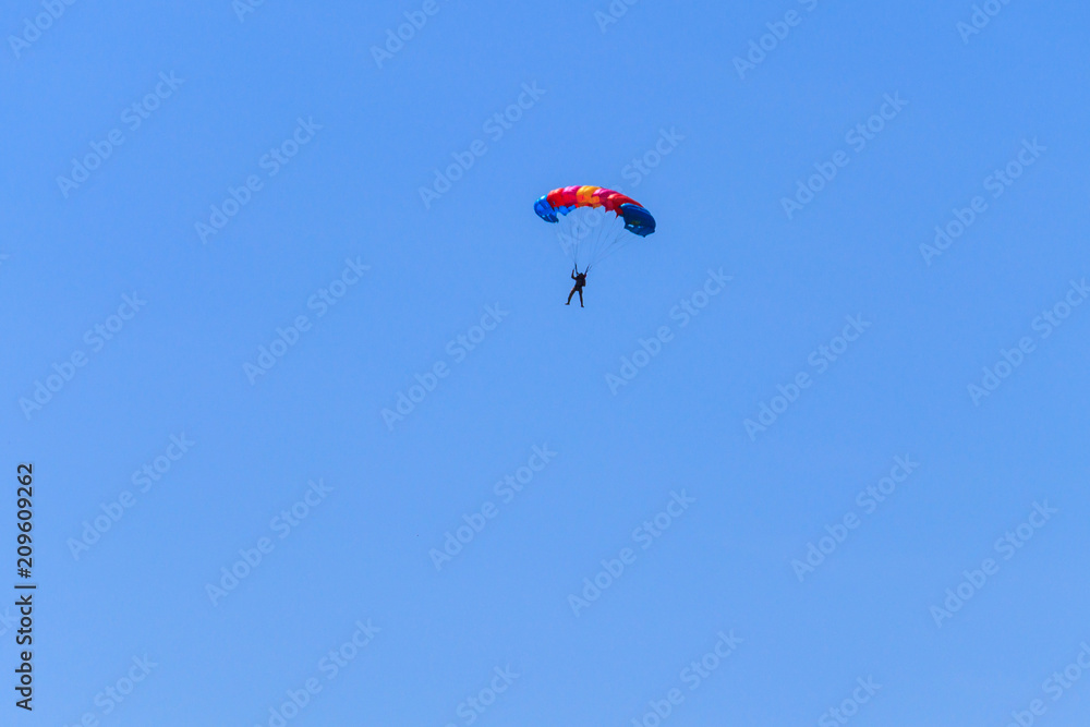 Parachutist descending with a parachute against blue sky Parachutist descending with a parachute against blue sky