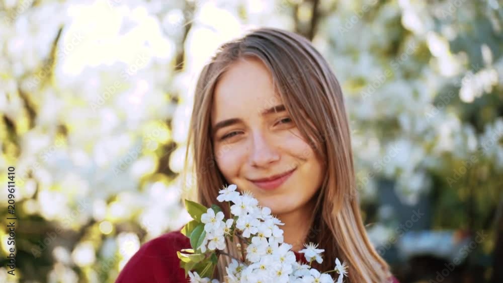 Cute Ukrainian young woman with blue eyes holding twigs with white flowers, looking at camera and smiling. Likable girl in the garden. Feminine image. Cute Ukrainian young woman with blue eyes holding twigs with white flowers, looking at camera and smiling. Likable girl in the garden. Feminine image.