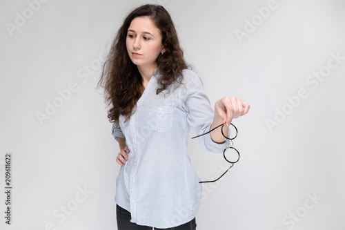 Portrait of a young girl. Beautiful young girl on a gray background. The girl is holding glasses in her hands. The girl refuses glasses. photo