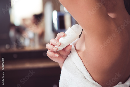 Close up of female hand preventing skin from perspiring. Girl is standing and holding antiperspirant in hand while rolling it on body photo