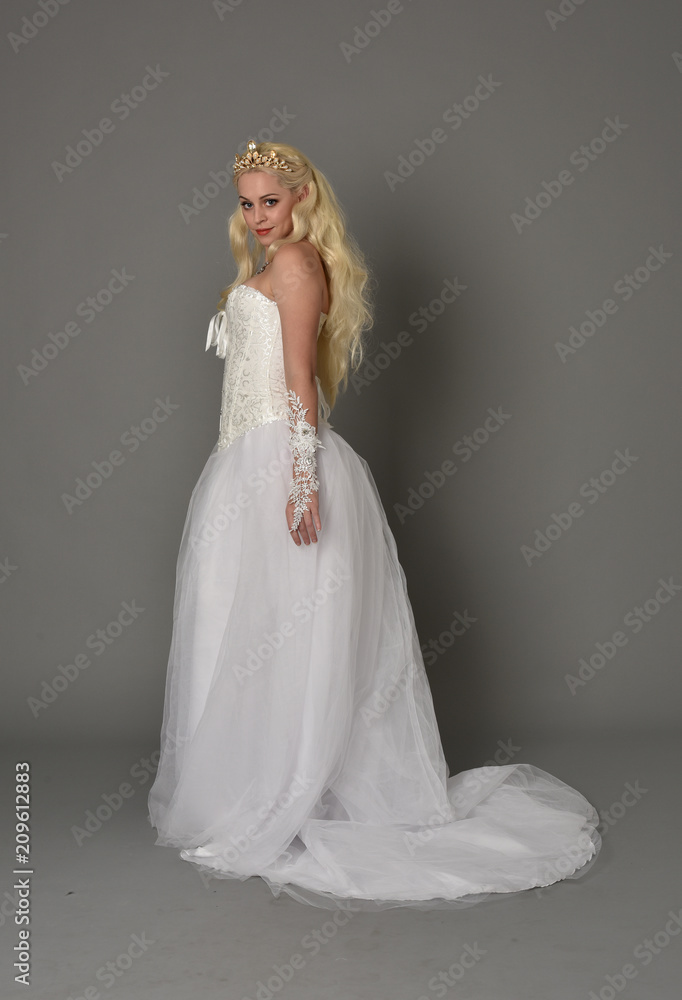 full length portrait of blonde girl wearing white fantasy gown. standing pose in side profile, grey studio background. full length portrait of blonde girl wearing white fantasy gown. standing pose in side profile, grey studio background.