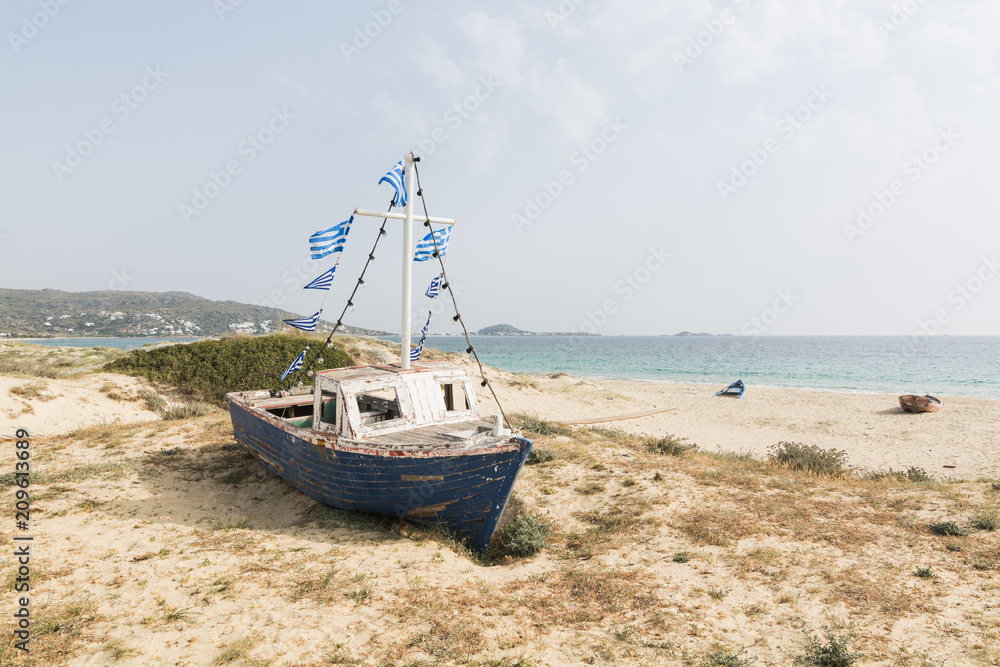 Old wooden fishing boat on the beach with Greek flags on the mast. Naxos island, Greece