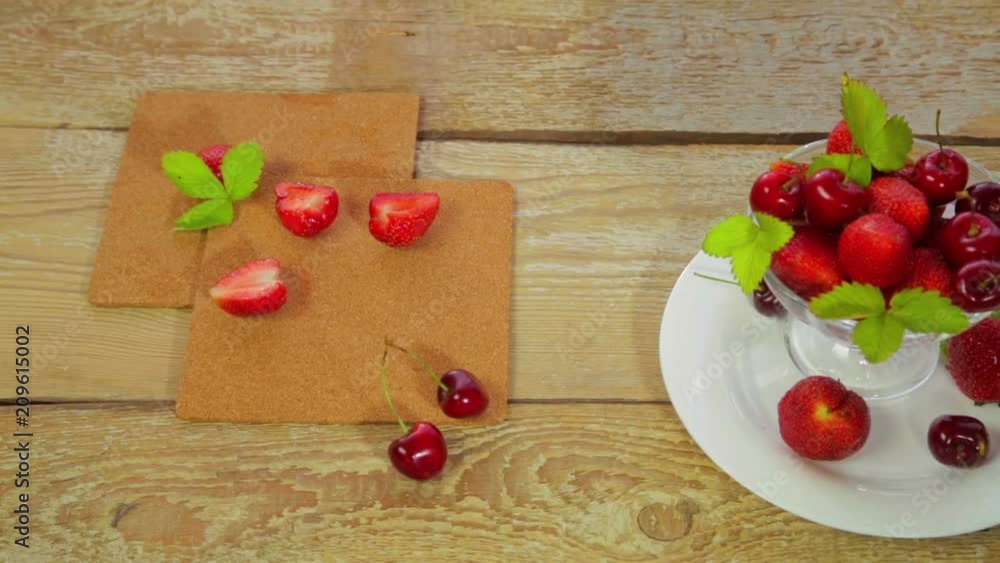 On a white plate that lies on a light wooden table is strawberry and cherry, close-up. The camera moves on dolly from left to right On a white plate that lies on a light wooden table is strawberry and cherry, close-up. The camera moves on dolly from left to right