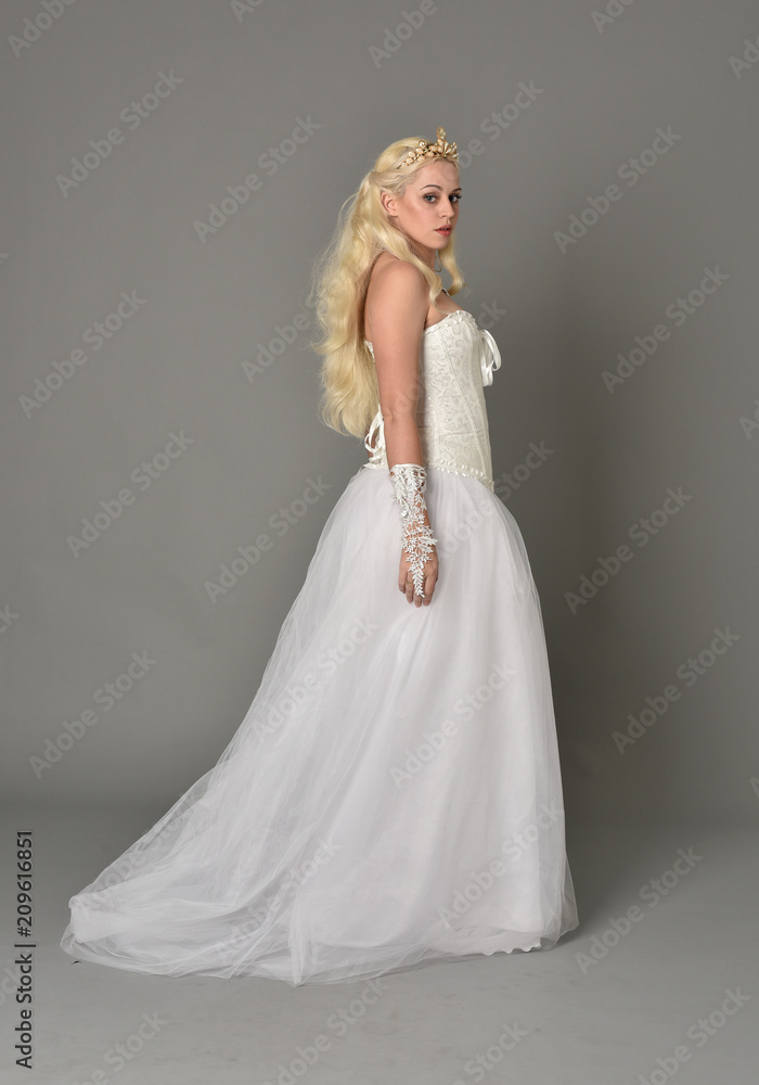 full length portrait of blonde girl wearing white fantasy gown. standing pose in side profile, grey studio background. full length portrait of blonde girl wearing white fantasy gown. standing pose in side profile, grey studio background.
