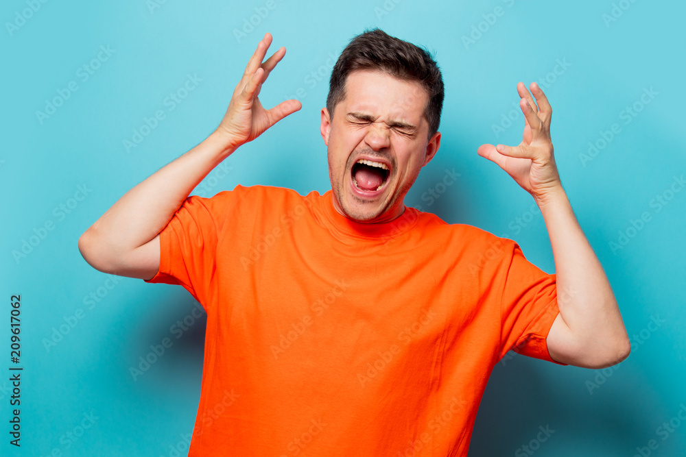 Young handsome man in orange t-shirt. Studio image on blue background