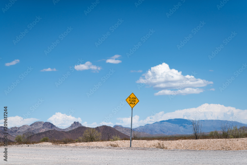 Flash flood warning sign in a dry desert with an unpaved road in the foreground and desert flora, a mountain, blue skies with puffy clouds in the background somewhere between California and Arizona Flash flood warning sign in a dry desert with an unpaved road in the foreground and desert flora, a mountain, blue skies with puffy clouds in the background somewhere between California and Arizona