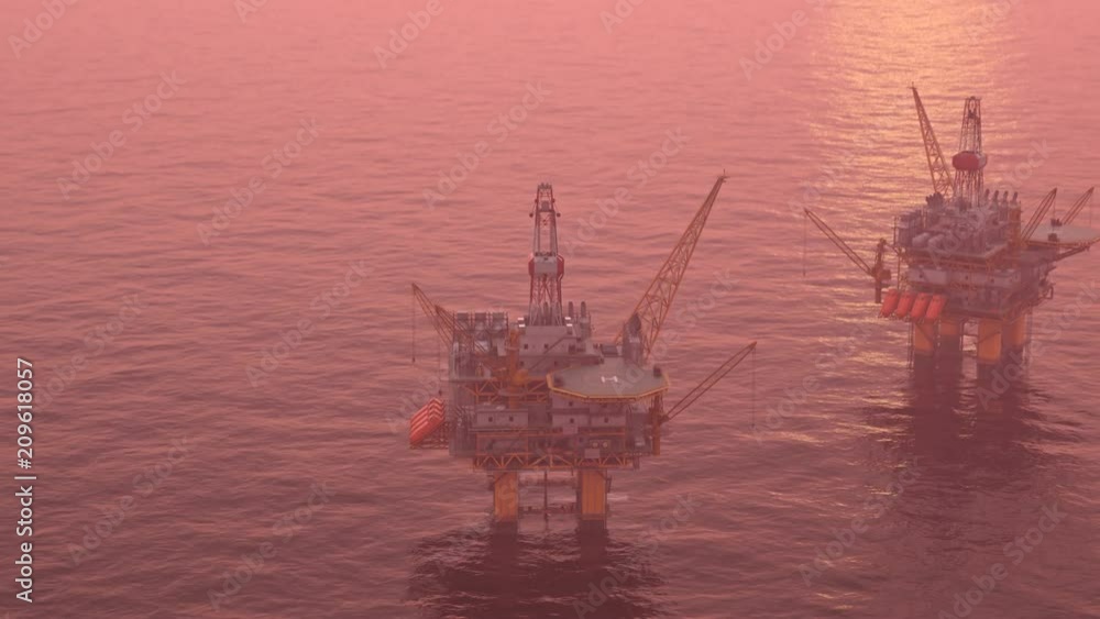 Two offshore platforms in the open sea with a pink evening sky and setting sun.