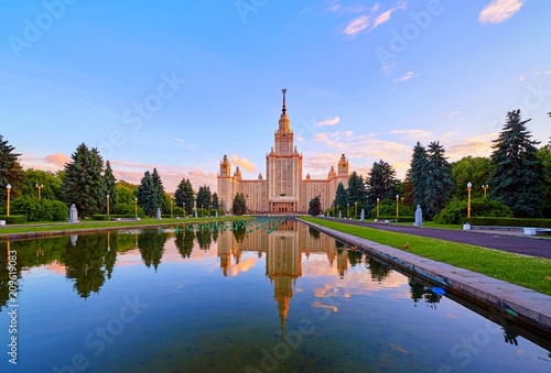 Wide angle vibrant panoramic view of sunset Moscow university campus under dramatic sky in spring with water reflections and red ducks