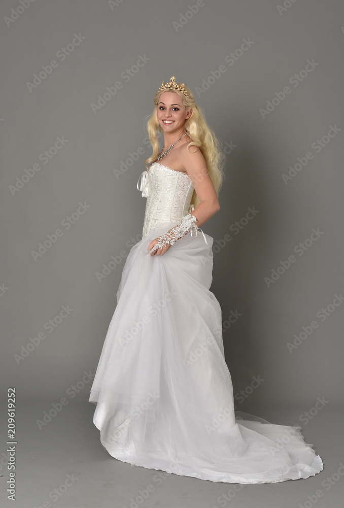 full length portrait of blonde girl wearing white fantasy gown. standing pose in side profile, grey studio background. full length portrait of blonde girl wearing white fantasy gown. standing pose in side profile, grey studio background.