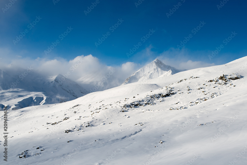 landscape of  gentle slope with rocks against a background of snow-capped mountains with clouds