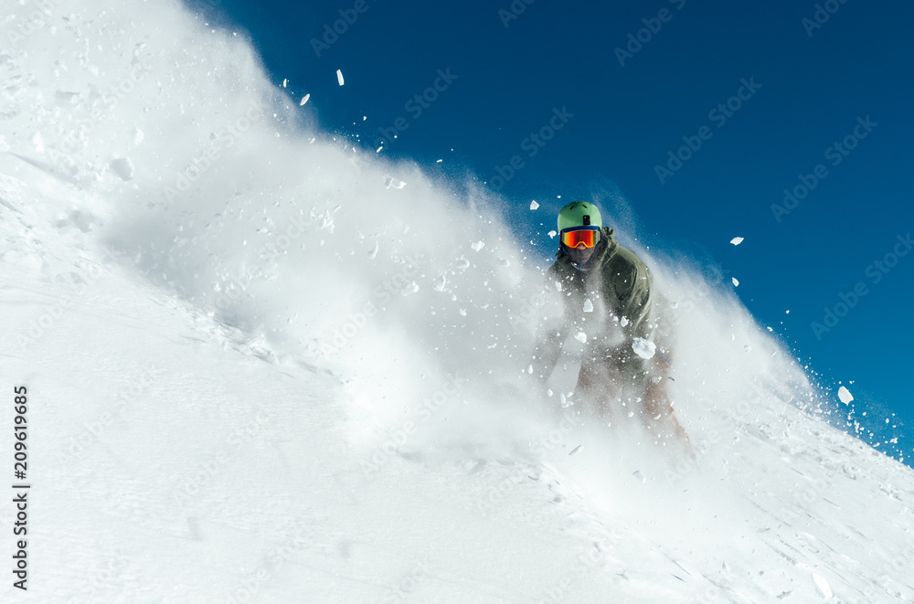 male snowboarder curved and brakes spraying loose deep snow on  freeride slope