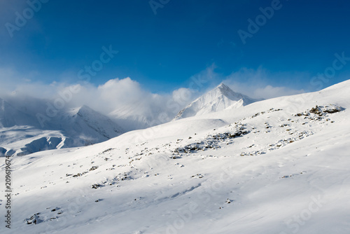 landscape of gentle slope with rocks against a background of snow-capped mountains with clouds