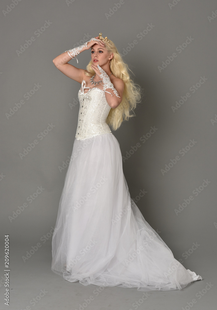 full length portrait of blonde girl wearing white fantasy gown. standing pose in side profile, grey studio background. full length portrait of blonde girl wearing white fantasy gown. standing pose in side profile, grey studio background.