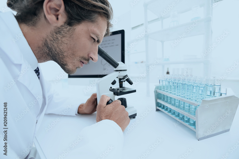 Young laboratory scientist looking at microscope in laboratory Young laboratory scientist looking at microscope in laboratory