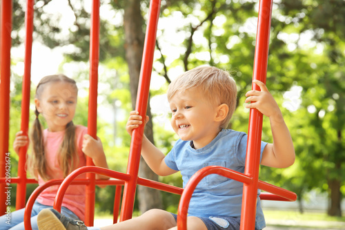 Cute little children playing on swings in park