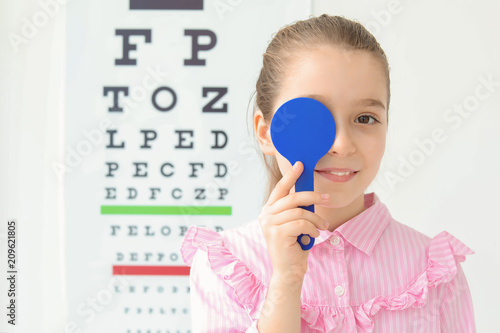 Cute little girl near eye chart in ophthalmologist office