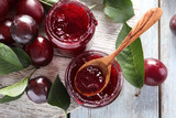 Glass jars with delicious plum jam on wooden background