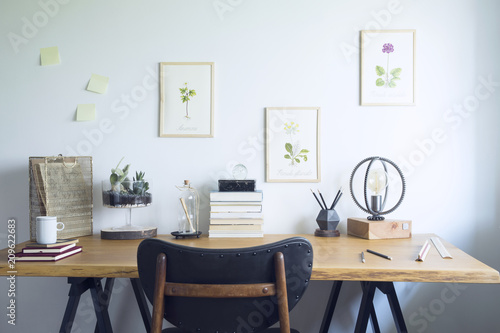 Modern home office interior with wooden desk, books,poster illustrations of plants, table lamp and office accessories. Stylish creative and vintage desk. © FollowTheFlow
