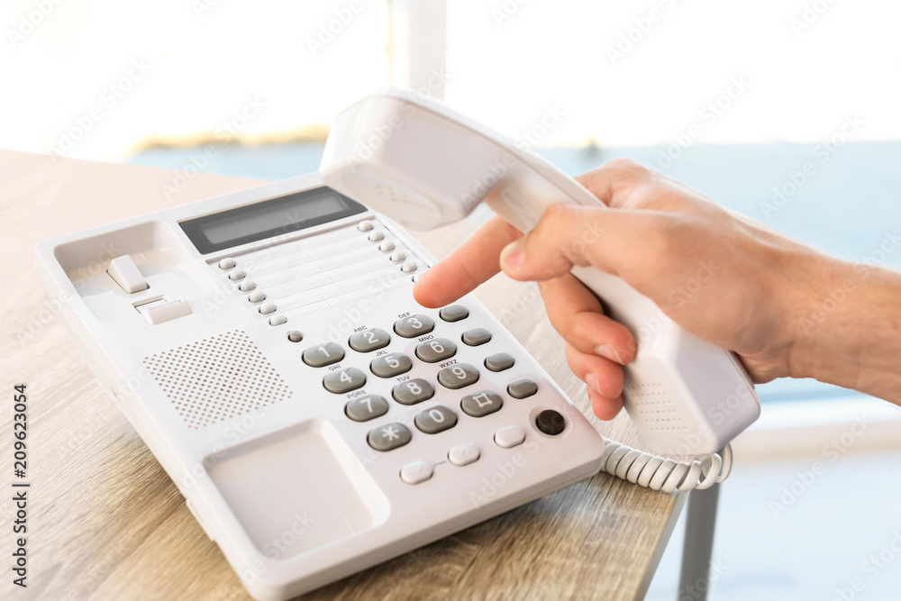Man dialing number on telephone at table indoors Man dialing number on telephone at table indoors