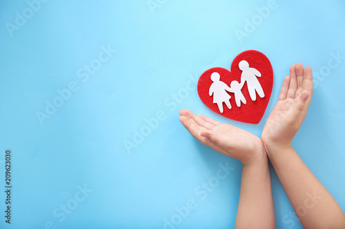 Child protecting red heart with paper silhouette of people on color background, top view