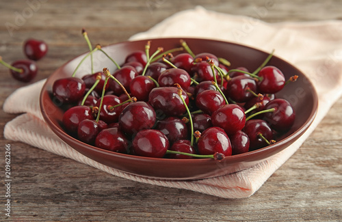 Plate with sweet red cherries on wooden table