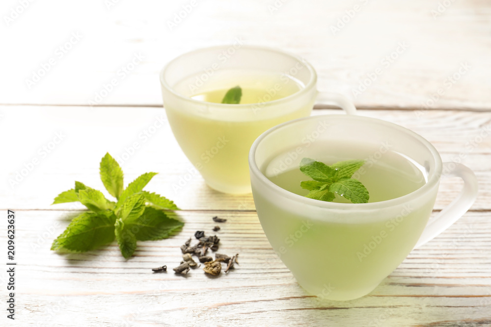 Cups with hot aromatic mint tea, fresh and dry leaves on wooden table Cups with hot aromatic mint tea, fresh and dry leaves on wooden table