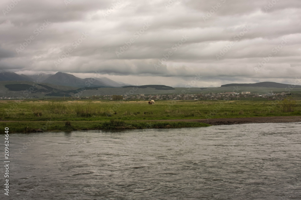 water, two horses, villages, mountains and clouds