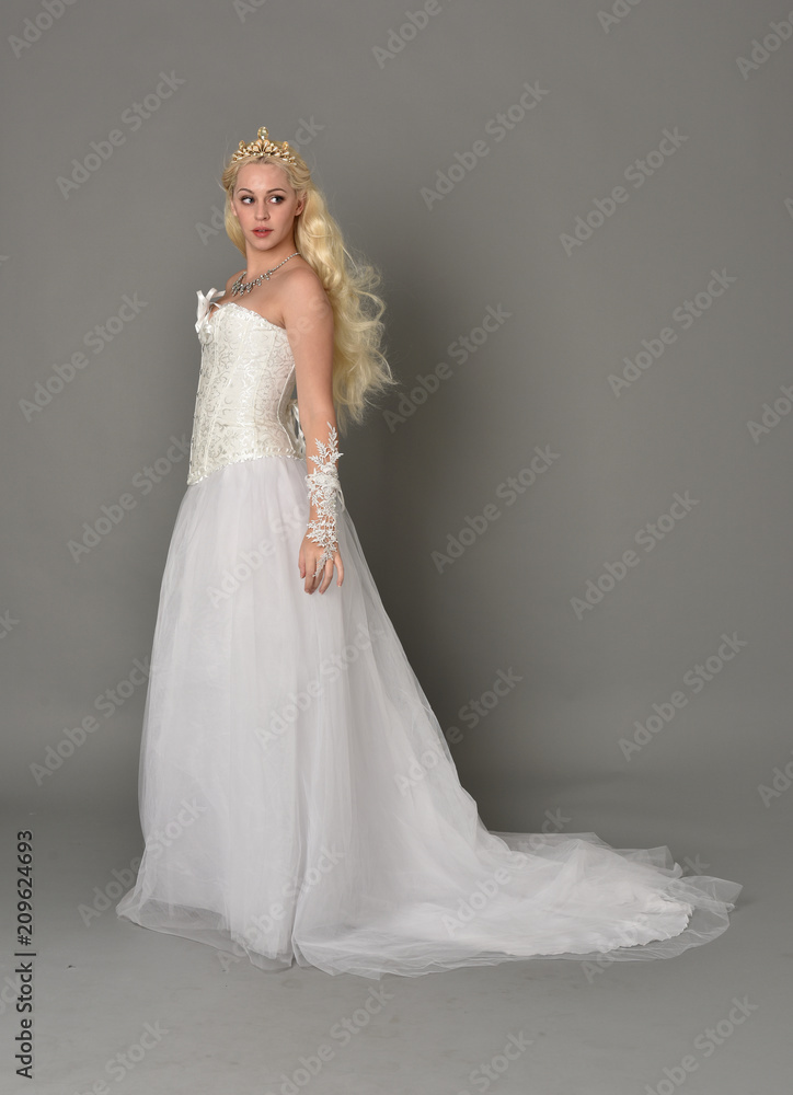 full length portrait of blonde  girl wearing white fantasy gown. standing pose in side profile, grey studio background.