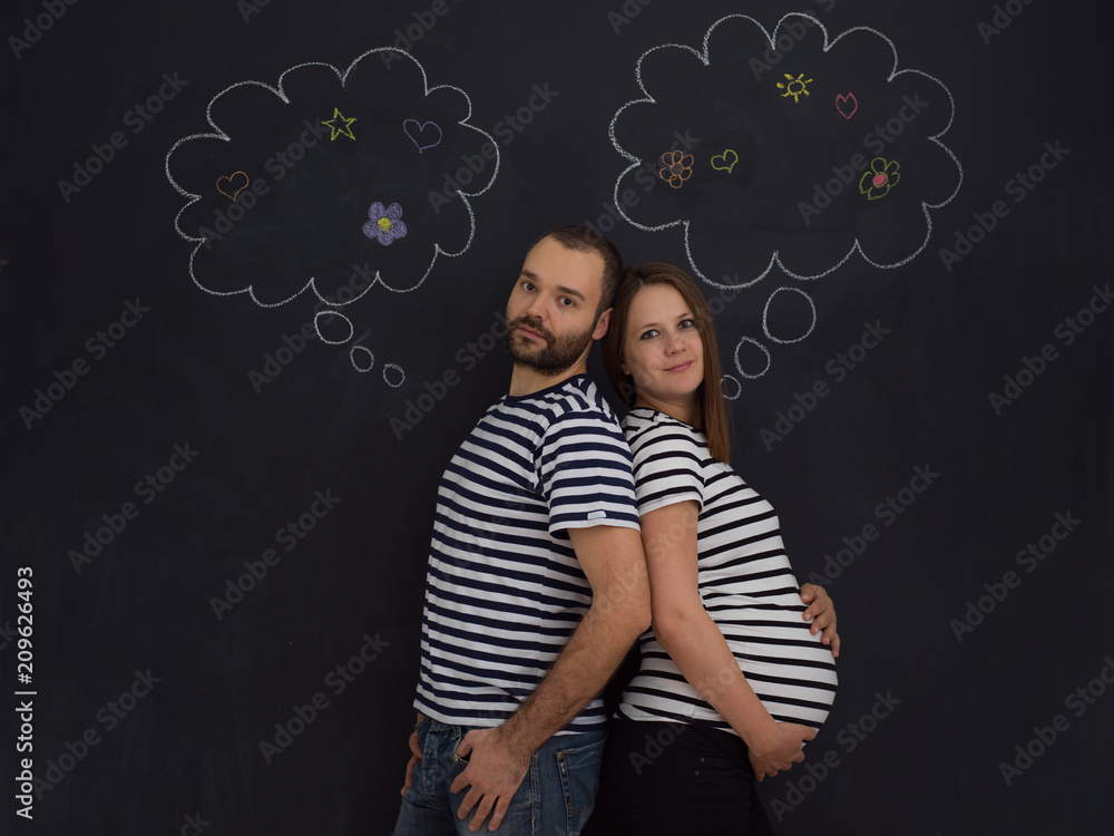 pregnant couple posing against black chalk drawing board