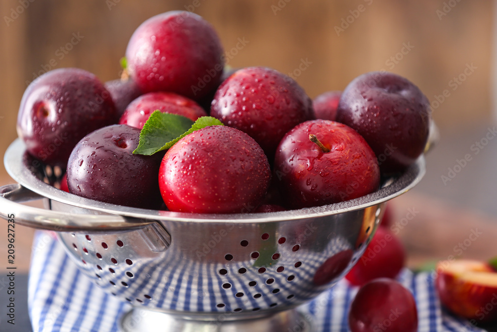 Colander with ripe juicy plums on table