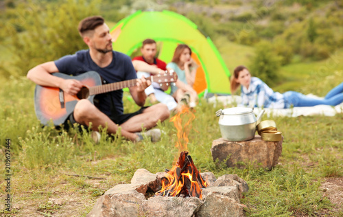 Group of people resting outdoors, focus on bonfire. Camping season