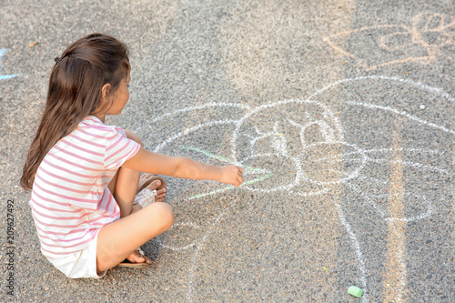 Cute little girl drawing with chalk on asphalt, outdoors