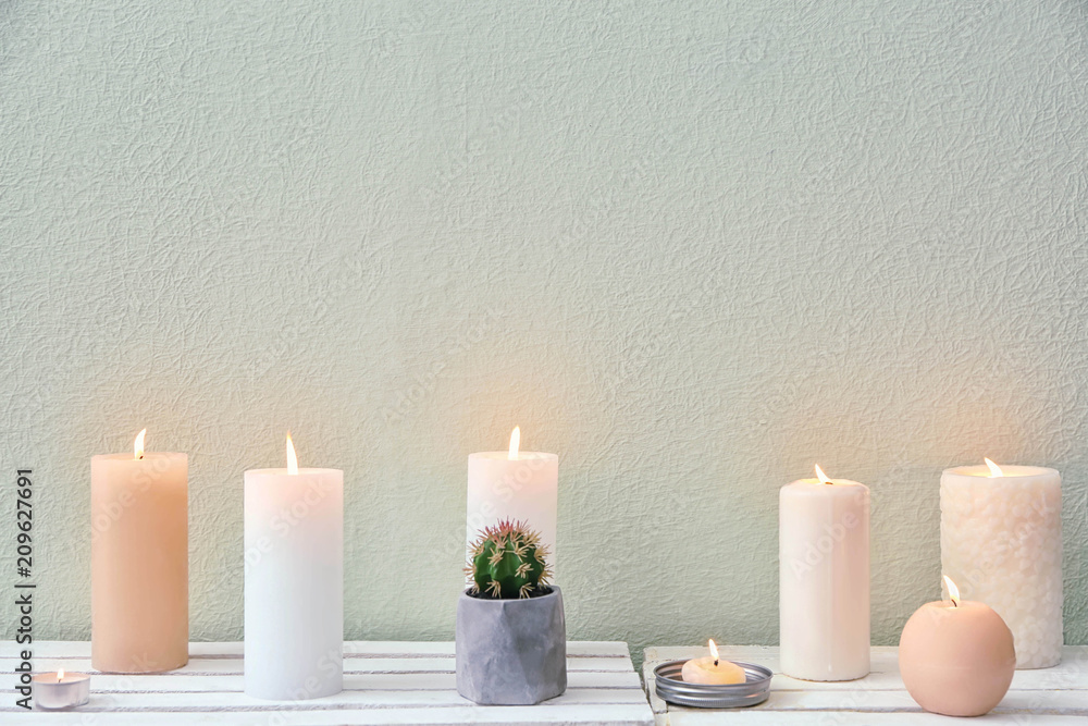 Beautiful burning candles on table against color background Beautiful burning candles on table against color background