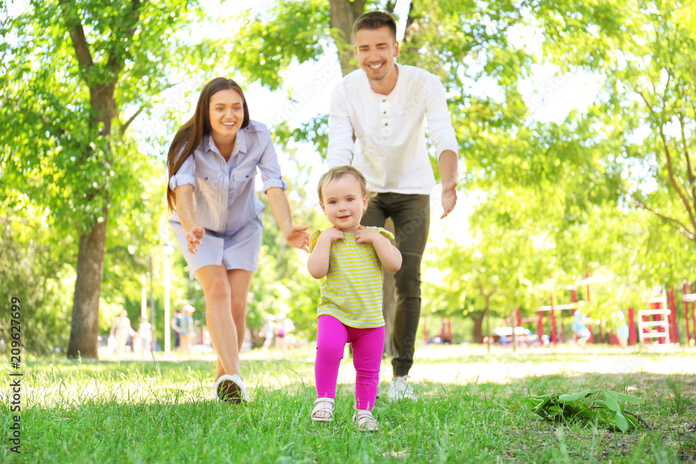 Fototapeta premium Parents supporting their baby daughter while she learning to walk outdoors