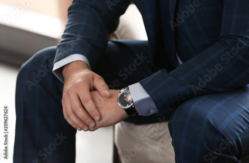 Young man in elegant suit sitting on sofa indoors