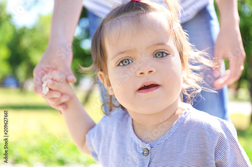 Adorable baby girl holding mother's hand while learning to walk outdoors