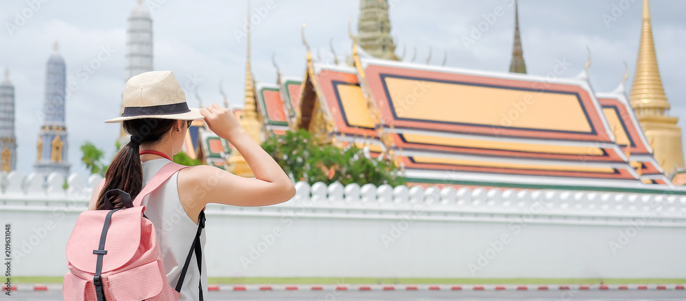 Young Woman traveling backpacker with hat, Asian hipster traveler looking to Wat Phra Kaew and Grand Palace of Bangkok, landmark and popular for tourist attractions in Thailand. Travel concept