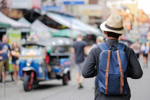 Young man traveling with hat, Asian hipster traveler walking at famous backpacker street in Bangkok (Khao San road), landmark and popular for tourist attractions in Thailand. Travel concept