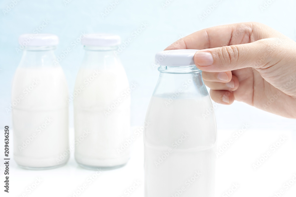 Hand's woman holding a bottle cap of milk isolated on white table. Three glass bottle of milk with blue background. with copy space for text. Hand's woman holding a bottle cap of milk isolated on white table. Three glass bottle of milk with blue background. with copy space for text.