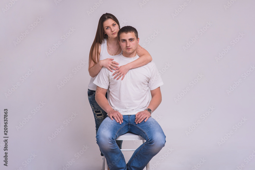 Portrait of a beautiful brunette girl and a young guy in a chair on a white background in family happiness Portrait of a beautiful brunette girl and a young guy in a chair on a white background in family happiness