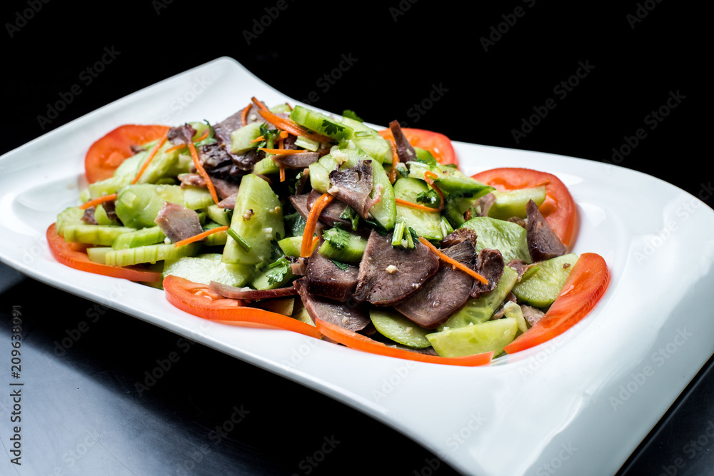 Chinese cuisine, boiled beef with cucumber and tomato in white plate on black background Chinese cuisine, boiled beef with cucumber and tomato in white plate on black background
