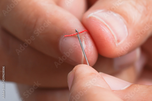 Close up hand holding the red threaded with stitching needle