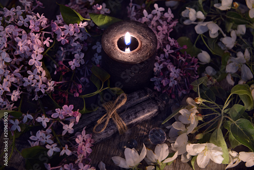 Lilac spring flowers with burning black candle. Occult, esoteric and divination still life. Halloween background with vintage objects and magic ritual