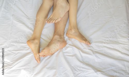 Feet of couple side by side in bed. Up view