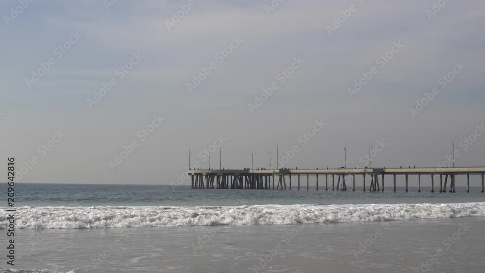 Static Medium Shot of the end of the Wooden Pier out in the ocean with a crowd of people milling on a nice sunny day at Manhattan Beach Static Medium Shot of the end of the Wooden Pier out in the ocean with a crowd of people milling on a nice sunny day at Manhattan Beach