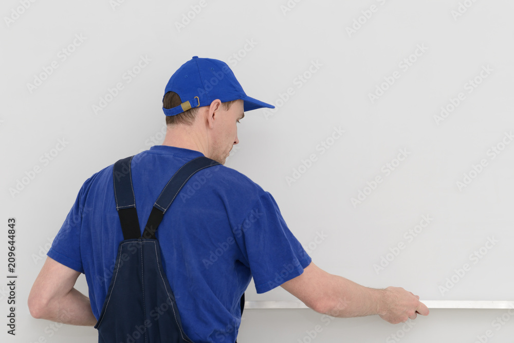worker in blue uniform measures the curvature of the wall with a level worker in blue uniform measures the curvature of the wall with a level