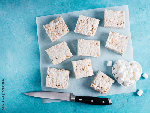 Homemade square bars of Marshmallow and crispy rice and ingredients on blue background. American dessert with marshmallow and crispy rice. Top view. Copy space photo